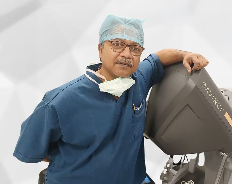Dr Udipta Ray in surgical scrubs, resting his arm on a da Vinci robotic surgical console